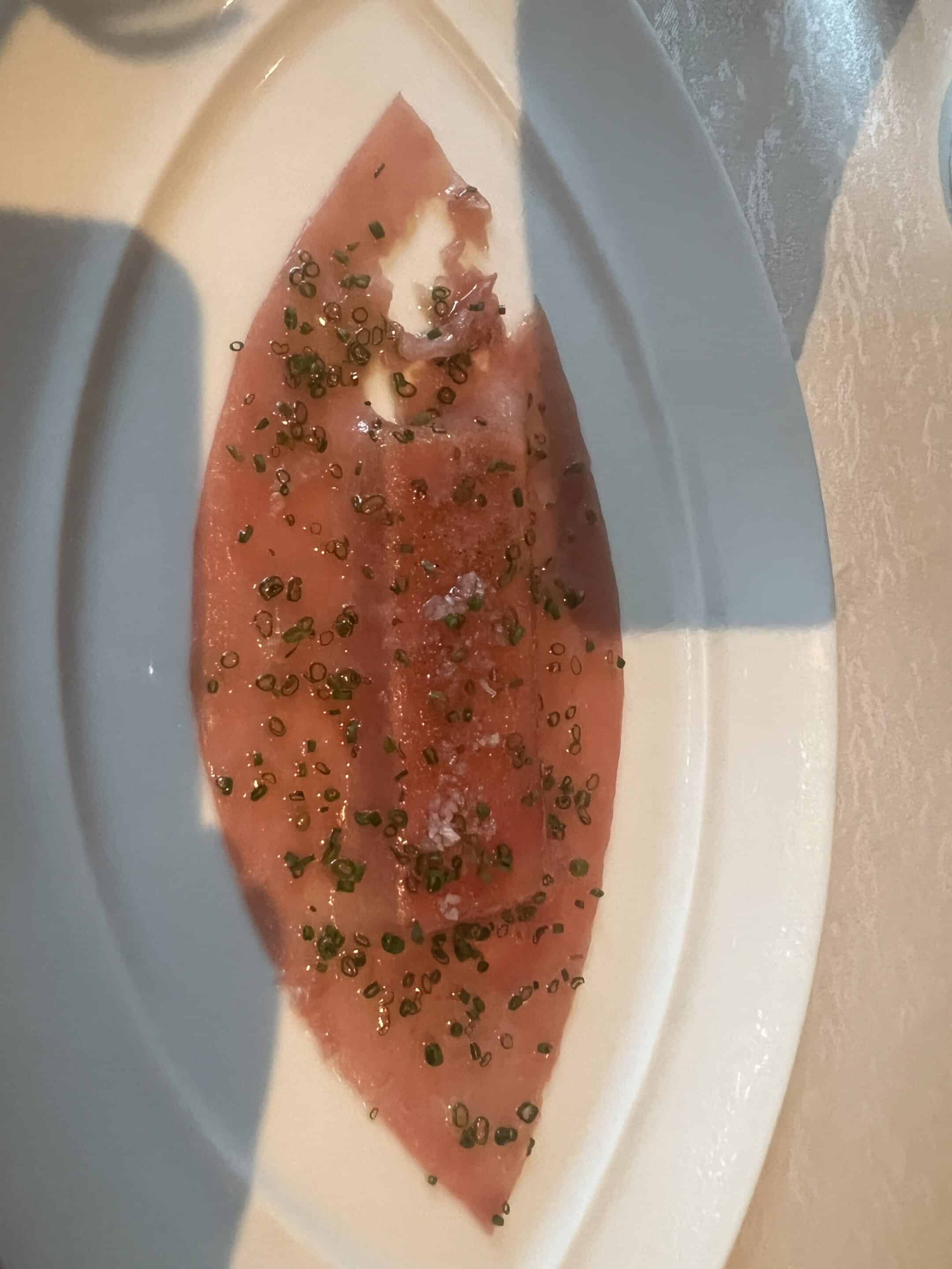 a piece of meat with green sprinkles on a white plate