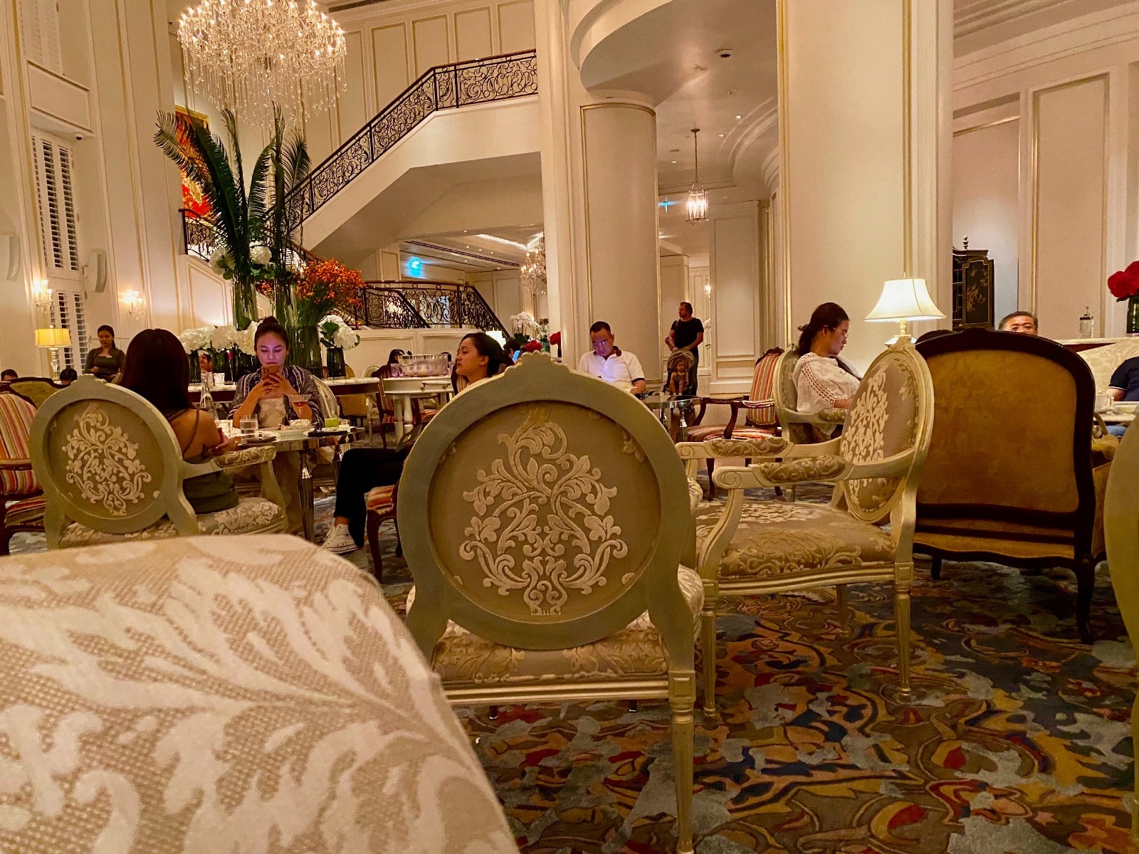 a group of people sitting at tables in a room with columns and stairs