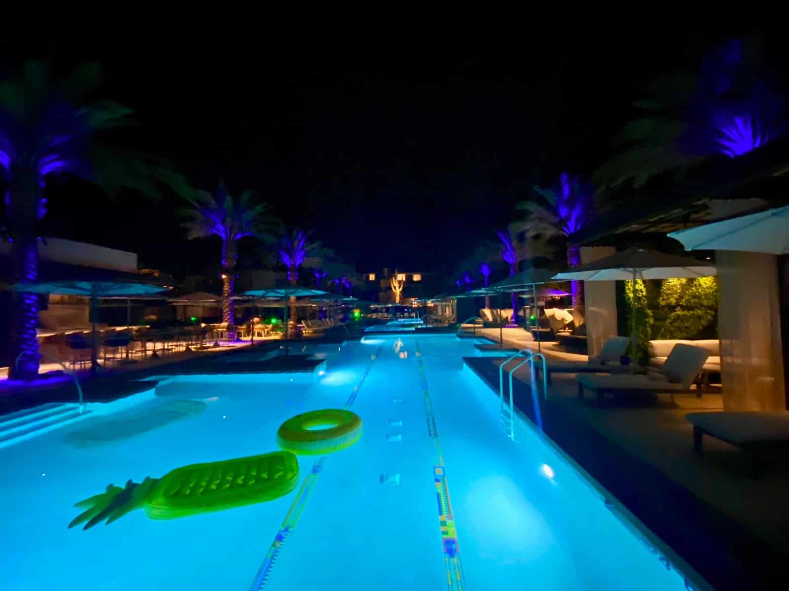 a pool with a floating raft and palm trees at night